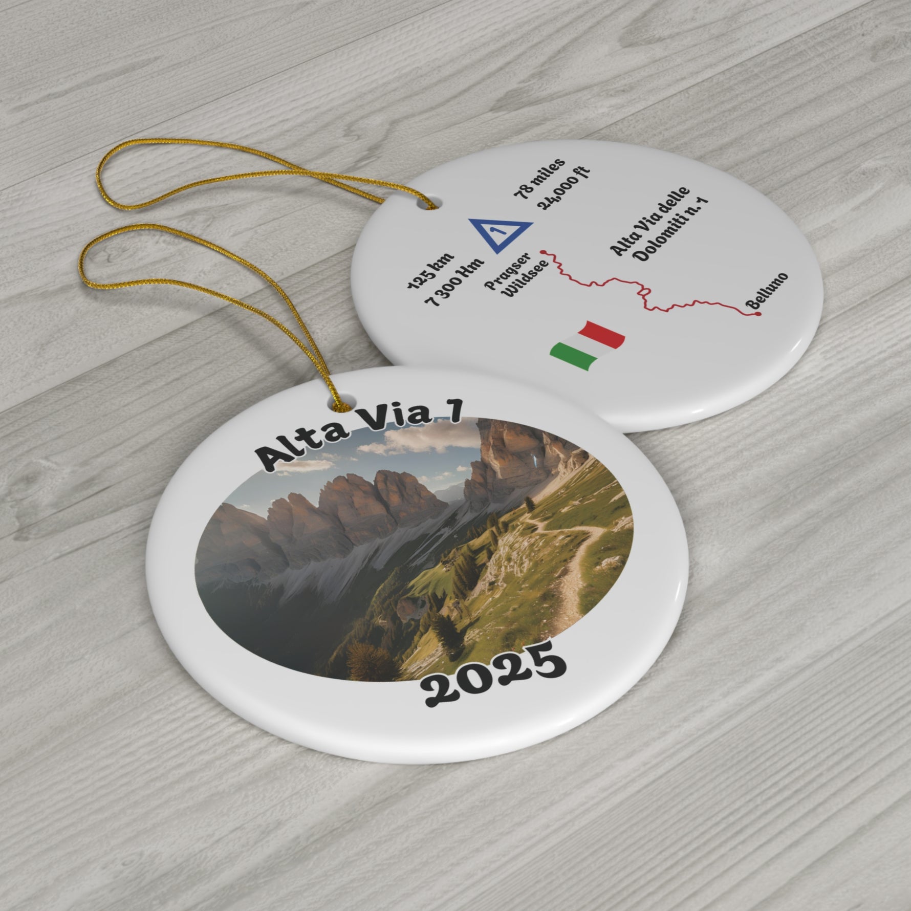 Alta Via 1 ceramic hiking ornament shown as flatlay on wooden surface, featuring front with landscape photo-version and back with customizable trail map.