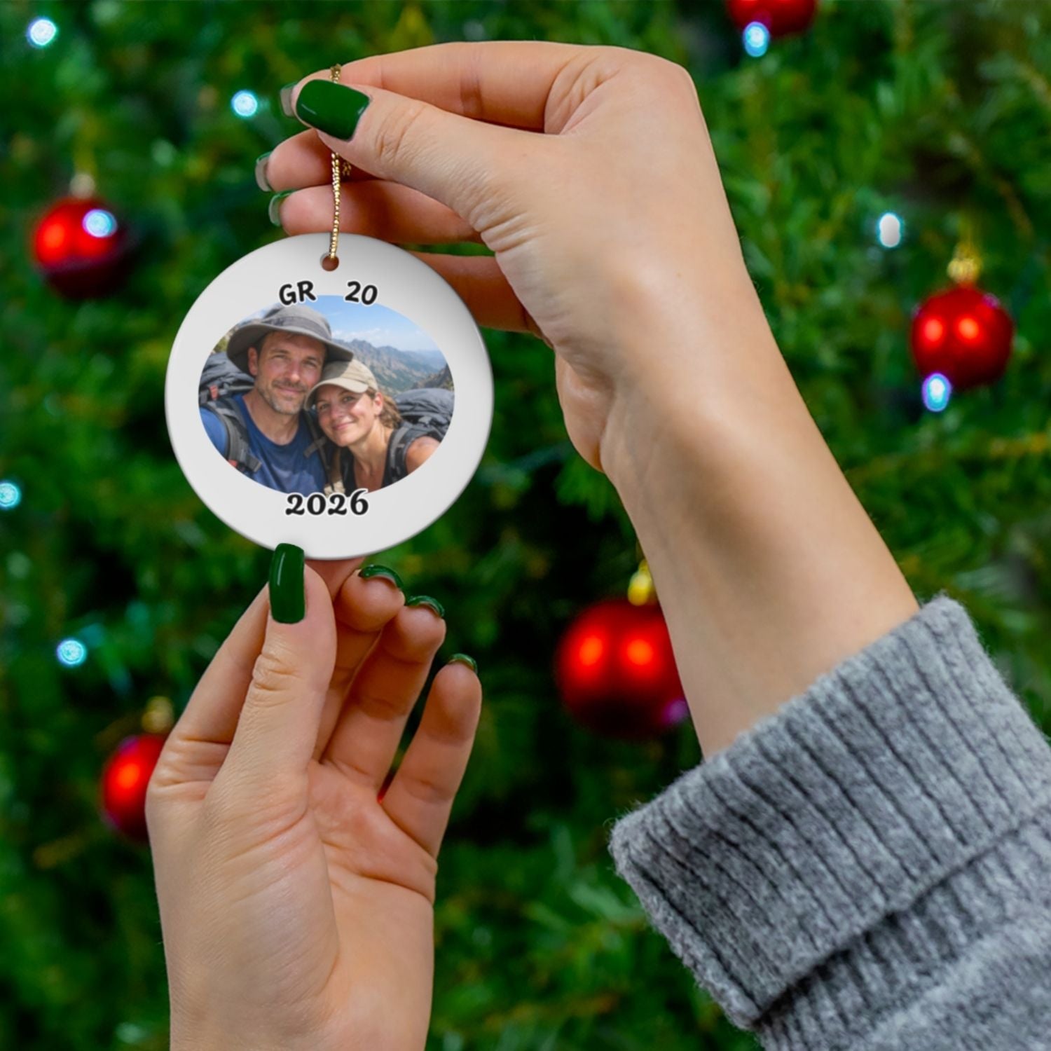 Personalized GR 20 ornament with custom hiking photo and year, held in hands in front of decorated Christmas tree.