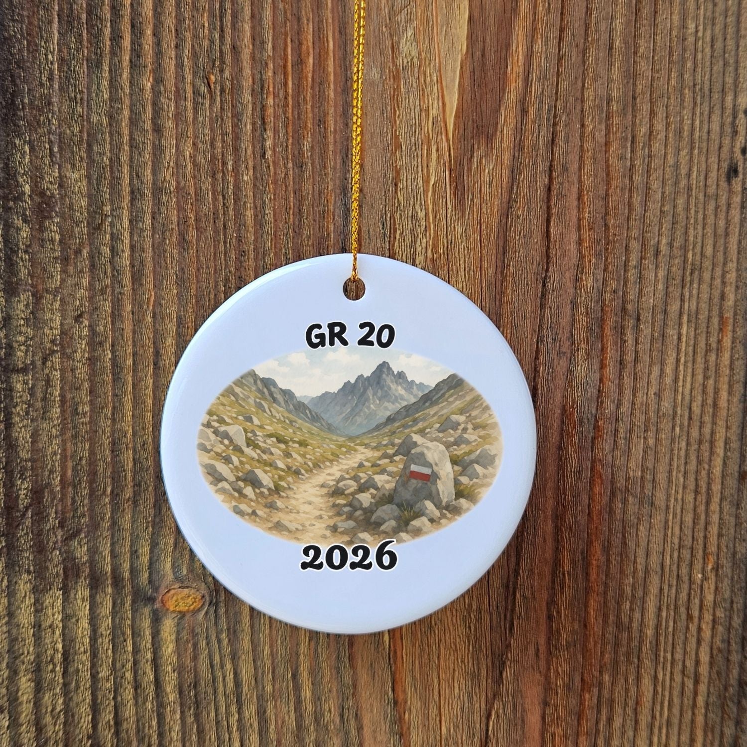 GR 20 ceramic keepsake with Corsican mountain trail watercolor and year 2025, shown hanging on rustic wood background.