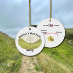 Front and back view of a round ceramic ornament with “Hadrian’s Wall Path 2025” and a gentle watercolor scene of the Sycamore Gap with and without the Sycamore. The back shows a trail map with 135 km / 84 miles and a Hadrians Wall miniature watercolor.