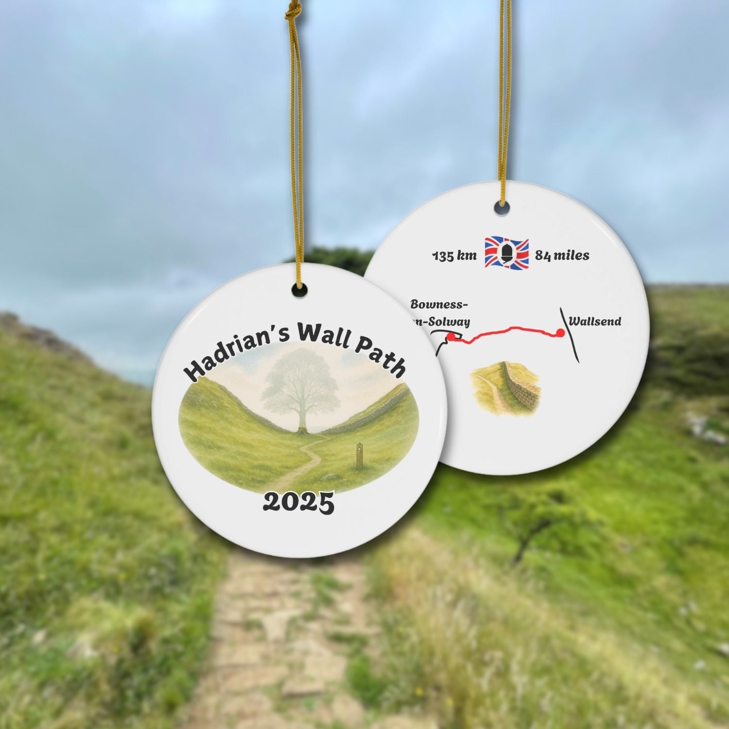 Front and back view of a round ceramic ornament with “Hadrian’s Wall Path 2025” and a gentle watercolor scene of the Sycamore Gap with and without the Sycamore. The back shows a trail map with 135 km / 84 miles and a Hadrians Wall miniature watercolor.