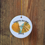 Caminito del Rey ornament hanging on a rustic wooden surface, highlighting its glossy ceramic finish and the gold hanging cord.